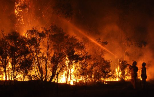 Firefighters spraying water at a large wildfire