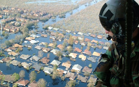A soldier looking out of a helicopter over a flooded town