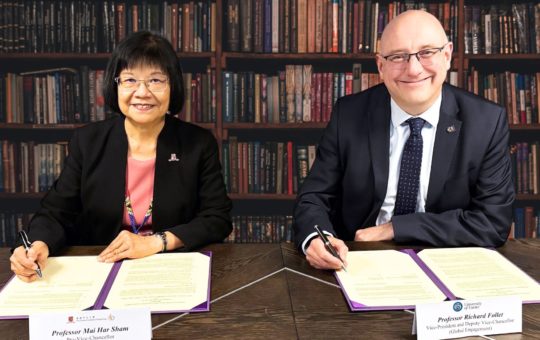 Two people sit at a desk signing forms