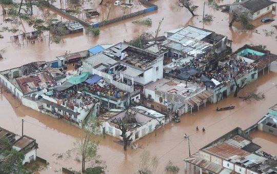 Large numbers of people on the roofs of buildings, surrounded by flood water
