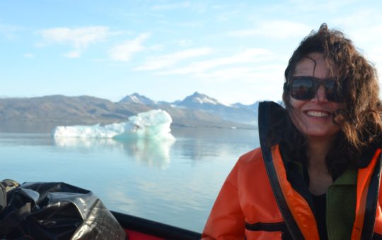 Angela Gallego-Sala in a boat, with water and ice visible behind, and land further in the distance