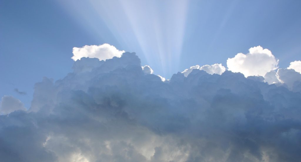 Beams of sunlight seen at the edges of white and grey clouds